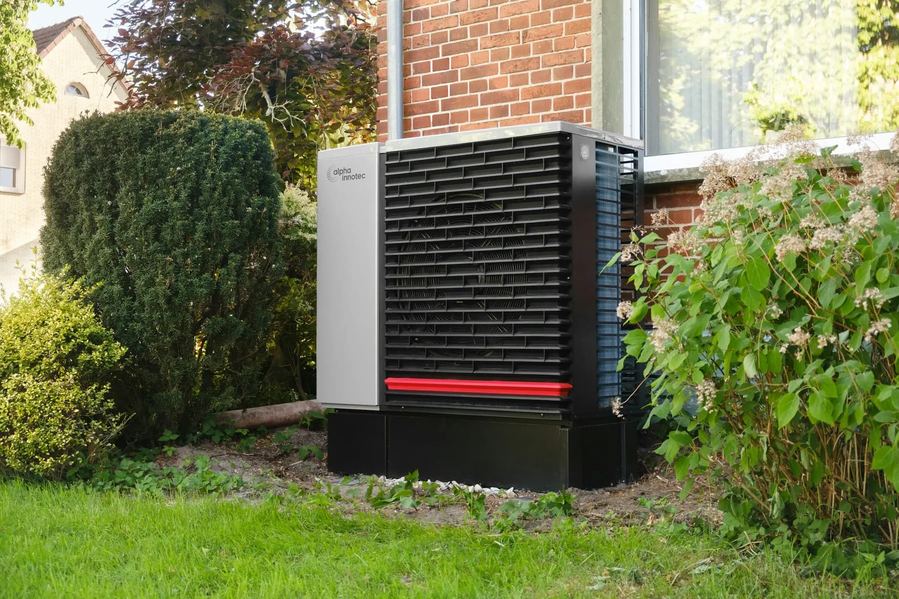 Pompe à chaleur air-eau installée dans un jardin, contre une façade en brique